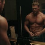 A shirtless Alan Ritchson looks at himself in a mirror in 'Reacher'.